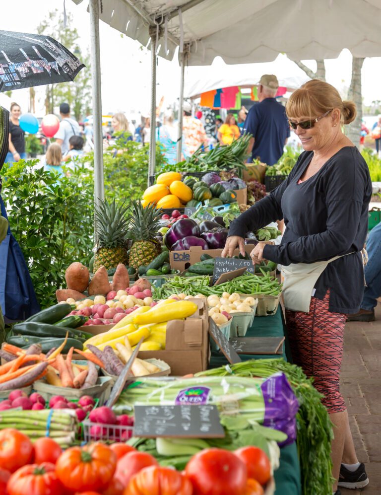 a lady looking at fruits and veggies at the farmers market