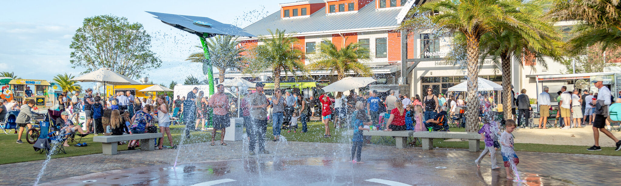 kids playing on splash pad surrounded by people and food trucks at an event